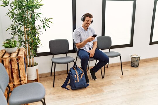 Young hispanic man listening to music sitting on chair at waiting room