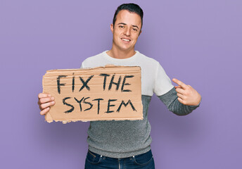 Handsome young man holding fix the system banner cardboard smiling happy pointing with hand and finger