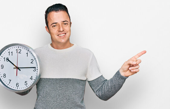 Handsome young man holding big clock smiling happy pointing with hand and finger to the side