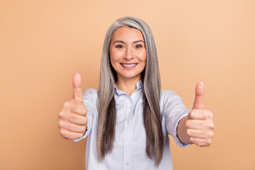 Photo of senior cheerful woman show fingers thumbs-up ideal select isolated over beige color...