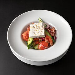 Fresh Greek salad - feta cheese, tomatoes, cucumber, red pepper, black olives and onion on a black background.