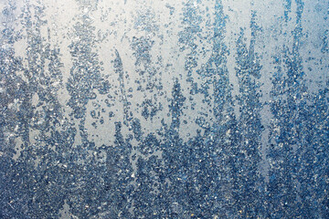 The texture of ice crystals and frozen water droplets on the window. Winter silver-blue background