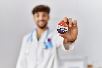 Young arab man wearing doctor uniform holding i voted badge at electoral college