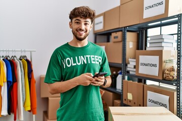 Young arab man wearing volunteer uniform using smartphone at charity center