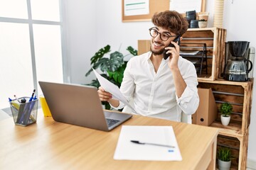 Young arab man talking on the smartphone reading document at office