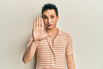 Handsome man wearing make up wearing casual t shirt doing stop sing with palm of the hand. warning expression with negative and serious gesture on the face.