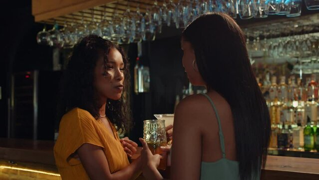 Biracial female friends sitting at bar drinking cocktails