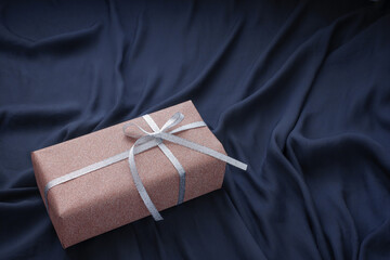 斜めアングルの紺の布の背景とピンクのラメのプレゼント
