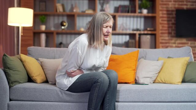 senior woman Suffer with stomach ache at home. Older female lying on the couch or bed in severe abdominal pain. Elderly mature adult woman person gastritis health problem. colon, or diarrhoea