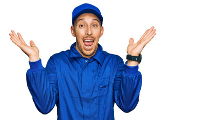 Naklejka premium Bald man with beard wearing builder jumpsuit uniform celebrating crazy and amazed for success with arms raised and open eyes screaming excited. winner concept