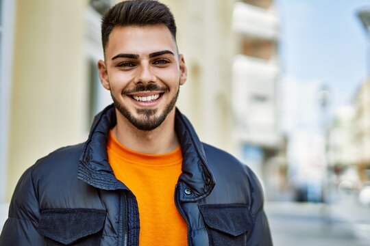 Handsome hispanic man with beard smiling happy and confident at the city wearing winter coat