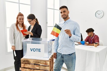 Young belgian voter man smiling happy holding belgium flag at vote center.