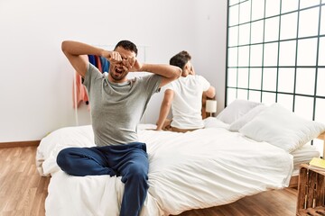 Two hispanic men couple waking up stretching arms and yawning at bedroom