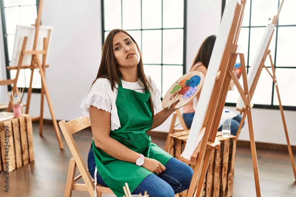 Sticker Young hispanic artist women painting on canvas at art studio looking sleepy and tired, exhausted for fatigue and hangover, lazy eyes in the morning.