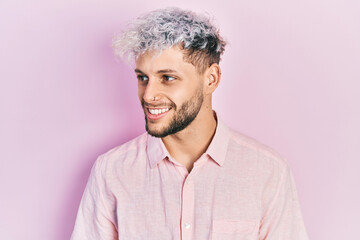 Young hispanic man with modern dyed hair wearing casual pink shirt looking to side, relax profile pose with natural face and confident smile.