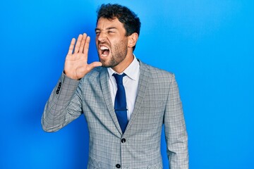 Handsome man with beard wearing business suit and tie shouting and screaming loud to side with hand on mouth. communication concept.