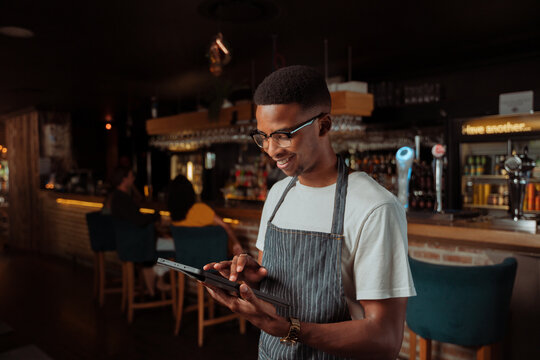 African American waiter working in restaurant holding digital tablet
