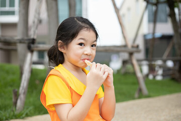 Happy asian girl in orange dress eating jelly candy.