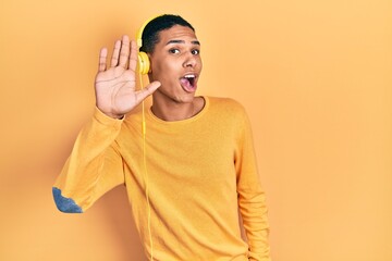 Young african american guy listening to music using headphones waiving saying hello happy and smiling, friendly welcome gesture © Krakenimages.com