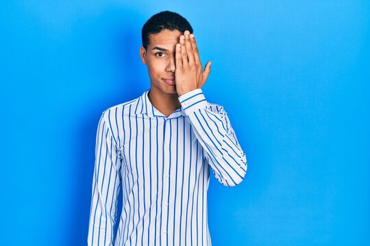 Young african american guy wearing casual clothes covering one eye with hand, confident smile on face and surprise emotion.