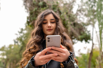 Beautiful woman browsing mobile phone while standing park on city. Successful businesswoman checks email on smartphone during a lunch break outside.