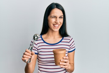 Young hispanic woman holding ice cream winking looking at the camera with sexy expression, cheerful...