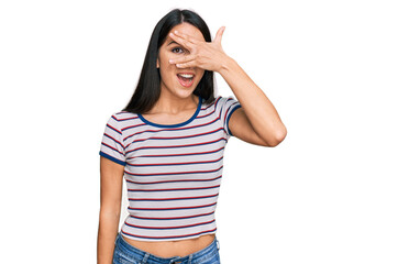 Obraz na płótnie Canvas Young hispanic girl wearing casual striped t shirt peeking in shock covering face and eyes with hand, looking through fingers with embarrassed expression.
