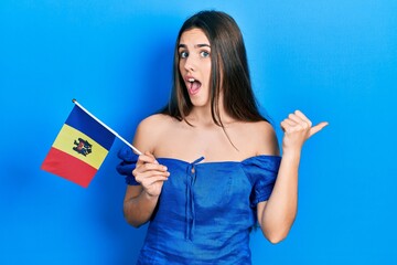 Fototapeta premium Young brunette teenager holding moldova flag pointing thumb up to the side smiling happy with open mouth