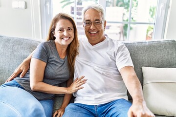 Middle age hispanic couple smiling happy and hugging sitting on the sofa at home.