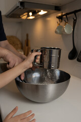 Dad and daughter cook in the home kitchen. Pour flour into a bowl, hands close-up.