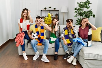 Fototapeta premium Group of young people watching football game wearing team scarf cheering game sitting on the sofa smiling happy doing ok sign with hand on eye looking through fingers
