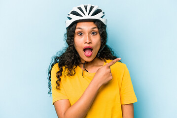 Young hispanic woman wearing a helmet bike isolated on blue background pointing to the side