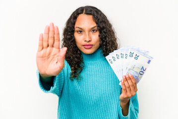 Young hispanic woman holding banknotes isolated on white background standing with outstretched hand showing stop sign, preventing you.