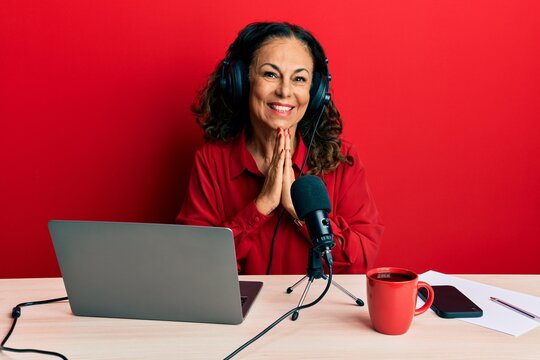Beautiful middle age woman working at radio studio praying with hands together asking for forgiveness smiling confident.