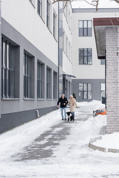 Couple in winter outfit walking border collie on leash on urban street.