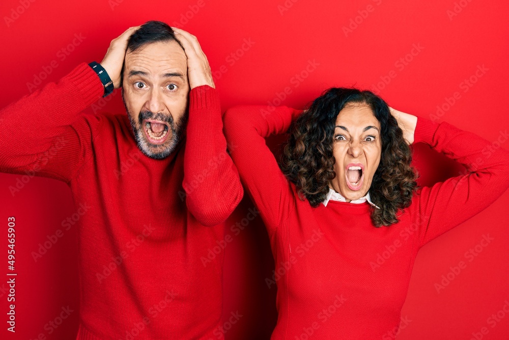 Poster Middle age couple of hispanic woman and man hugging and standing together crazy and scared with hands on head, afraid and surprised of shock with open mouth