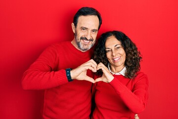 Middle age couple of hispanic woman and man hugging and standing together smiling in love doing heart symbol shape with hands. romantic concept.