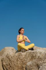 Naklejka na ściany i meble Woman doing yoga meditation sitting on rocks. Healthy mind and body.