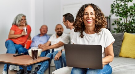 Group of middle age friends sitting on the sofa speaking. Woman smiling happy using laptop at home.