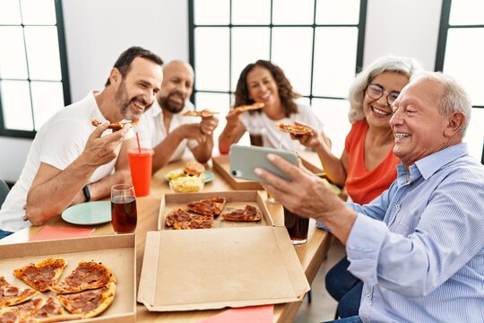 Group of middle age people smiling happy eating italian pizza make selfie by the smartphone at home