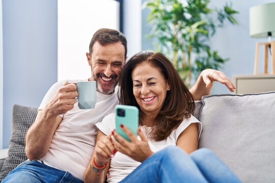 Middle age man and woman couple using smartphone and drinking coffee at home