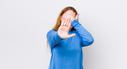 pretty red head woman covering face with hand and putting other hand up front to stop camera,...