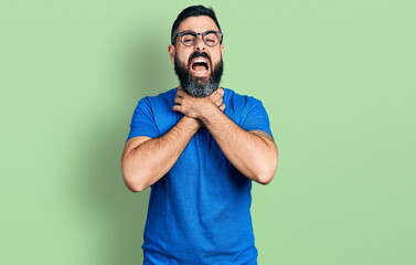 Hispanic man with beard wearing casual t shirt and glasses shouting and suffocate because painful strangle. health problem. asphyxiate and suicide concept.