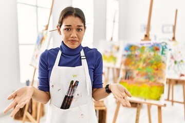 Young brunette woman at art studio clueless and confused with open arms, no idea concept.