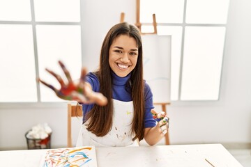 Young latin woman smiling confident showing painted palm hands at art studio