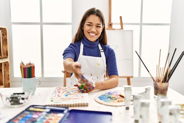 Young brunette woman at art studio with painted hands smiling friendly offering handshake as greeting and welcoming. successful business.