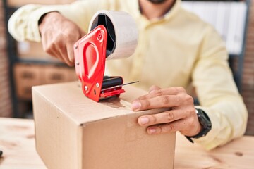 Young hispanic man ecommerce business worker packing cardboard box at office