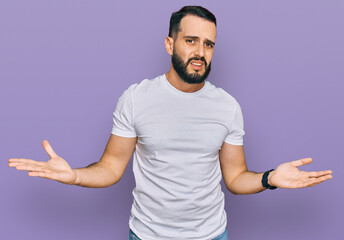 Fototapeta premium Young man with beard wearing casual white t shirt clueless and confused with open arms, no idea concept.