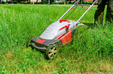 A man mows the grass with an electric lawn mower. Freshly mown grass.