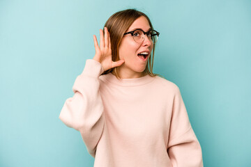 Young caucasian woman isolated on blue background trying to listening a gossip.